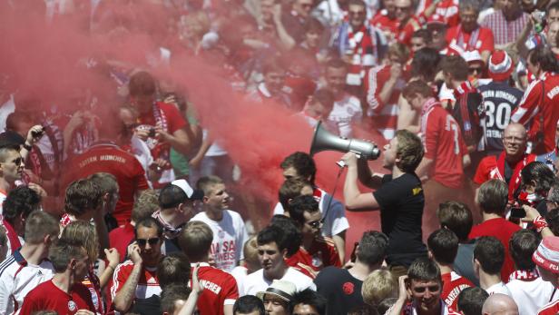 Eine Menschenmenge, vermutlich Fußballfans, inmitten von rotem Rauch und mit einem Megaphon.