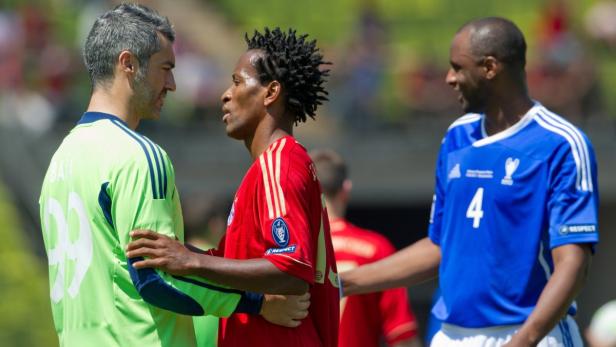 Drei Fußballspieler in Trikots stehen auf dem Spielfeld.