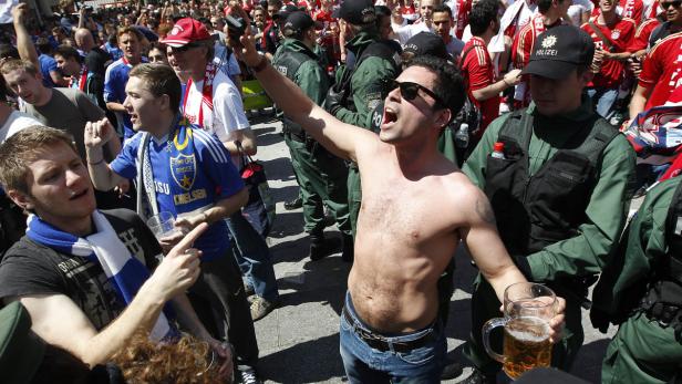 Ein Mann ohne Hemd jubelt mit einem Bierkrug in einer Menschenmenge, umgeben von Polizisten.