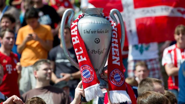 Ein aufgeblasener Pokal mit einem Schal des FC Bayern München wird in einer Menschenmenge hochgehalten.