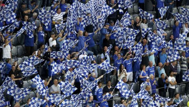 Eine Menschenmenge schwenkt blau-weiß karierte Chelsea FC-Flaggen auf einer Tribüne.