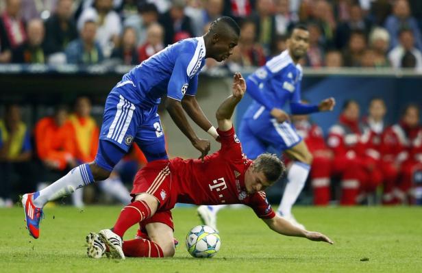 Ein Fußballspieler im roten Trikot liegt am Boden, während ein Spieler im blauen Trikot steht.