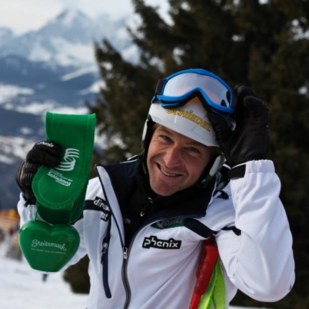 Ein lächelnder Skifahrer mit Helm und Skibrille hält eine grüne Steiermark-Herzdose in der Hand.