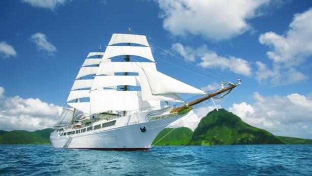 Das Segelschiff „Sea Cloud II“ fährt auf dem Meer vor einer grünen Insel.