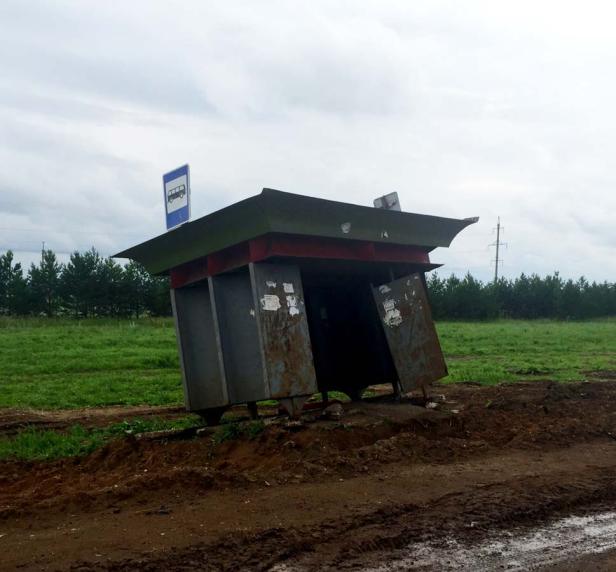 Eine heruntergekommene Bushaltestelle steht schief auf einem Feldweg.