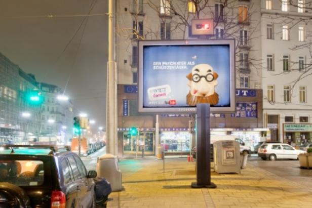 Pez/Rock+Partner/Gewista Ein Werbebildschirm auf einer Straße zeigt eine Karikatur mit der Aufschrift „Der Psychiater als Schürzenjäger“.