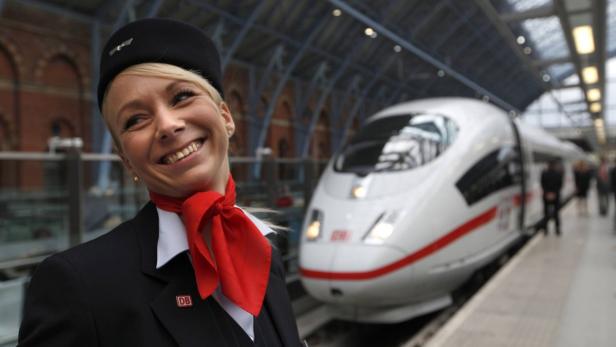 Eine lächelnde DB-Mitarbeiterin vor einem ICE-Zug am Bahnhof.