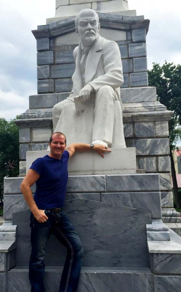 Ein Mann posiert neben einer Statue von Lenin.