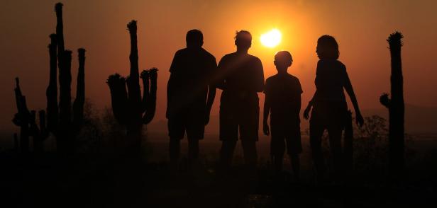Eine Familiengruppe steht bei Sonnenuntergang vor Kakteen in der Wüste.