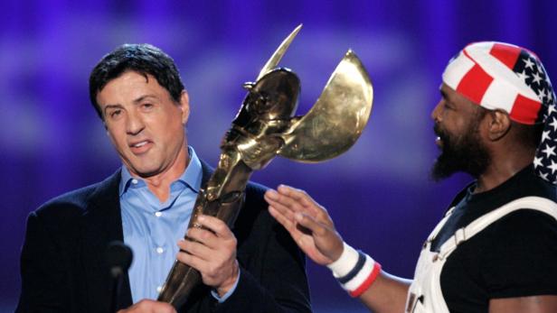 Sylvester Stallone hält eine goldene Trophäe, während Mr. T daneben steht.