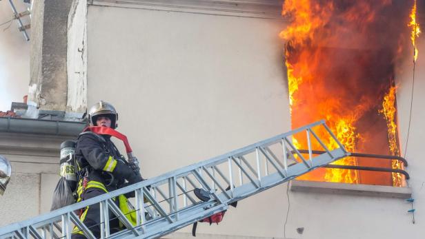 Ein Feuerwehrmann steht auf einer Leiter vor einem brennenden Fenster.