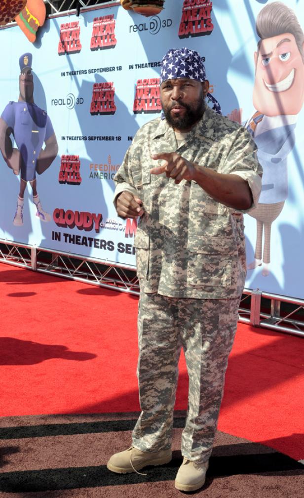 Ein Mann im Camouflage-Anzug posiert vor einem „Cloudy with a Chance of Meatballs“-Poster.