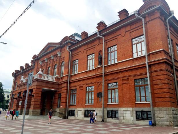 Ein großes, rotes Backsteingebäude mit klassischer Architektur und Passanten davor.