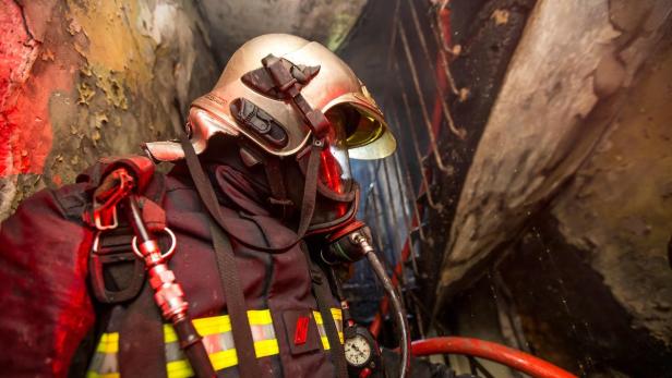Ein Feuerwehrmann mit Helm und Atemschutzmaske in einem verrauchten Gebäude.