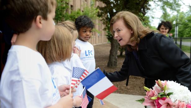 Eine Frau spricht mit einer Gruppe von Kindern, die französische und amerikanische Flaggen halten.