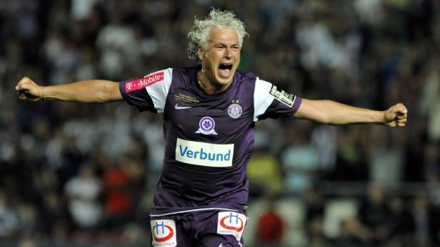 Ein jubelnder Fußballspieler mit grauen, lockigen Haaren im lila Trikot.