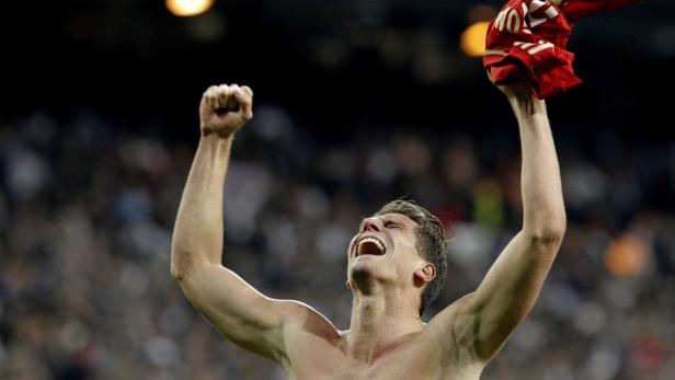 Ein jubelnder, barfüßiger Mann mit einem roten Trikot in der Hand feiert mit erhobenen Armen.