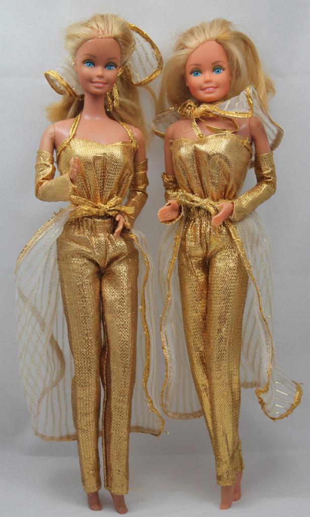 Zwei Barbie-Puppen tragen goldene Overalls mit passenden Accessoires.