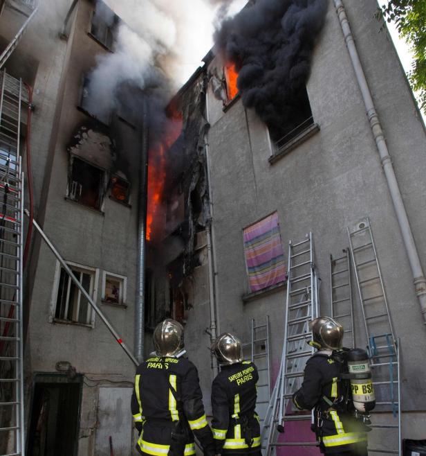 Drei Feuerwehrleute beobachten ein brennendes Gebäude in Paris.
