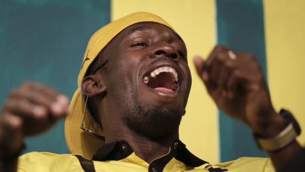 Ein lachender Mann mit gelber Kappe und gelbem Hemd gestikuliert.