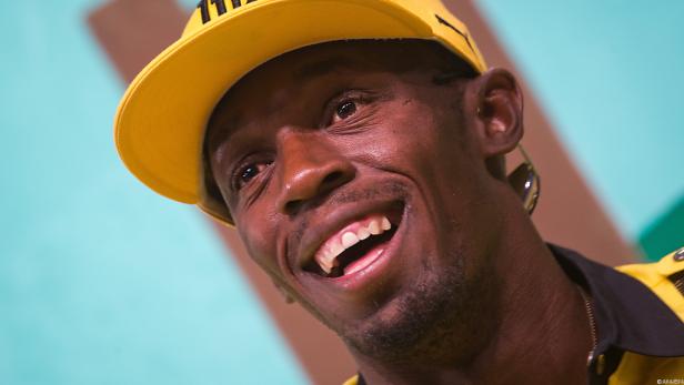 Usain Bolt lächelt in die Kamera und trägt eine gelbe Kappe.