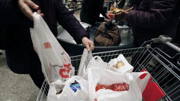 Ein Einkaufswagen gefüllt mit Plastiktüten an einer Supermarktkasse.
