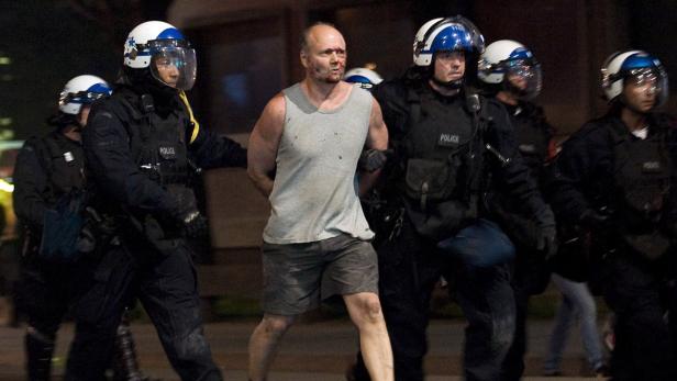 Ein Mann mit blutendem Gesicht wird von Polizisten in Schutzausrüstung abgeführt.
