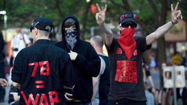 Mehrere Demonstranten, einige mit Bandanas, protestieren auf einer Straße.