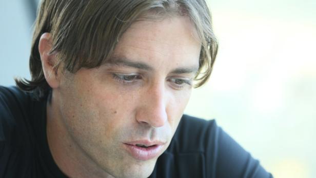 Ein Mann mit braunen Haaren und einem schwarzen T-Shirt schaut nach unten.