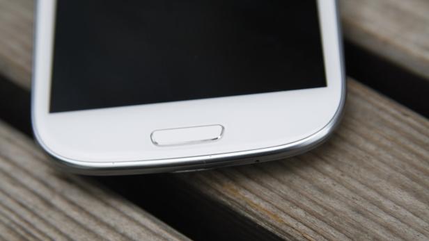 Ein weißes Smartphone liegt auf einer Holzoberfläche.