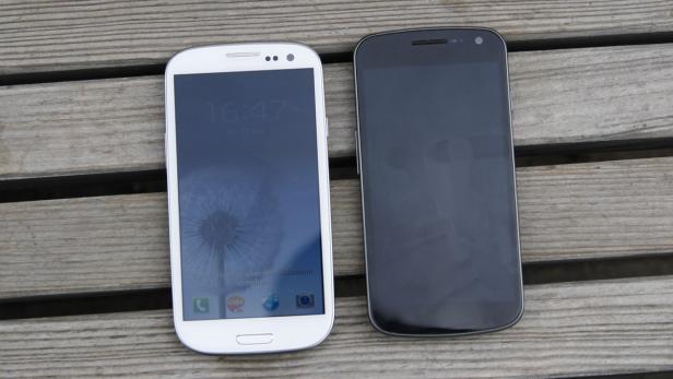 Zwei Smartphones, ein weißes und ein schwarzes, liegen auf einem Holztisch.