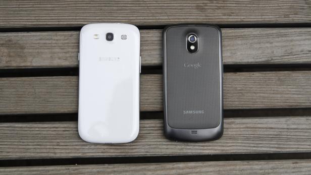 Ein weißes und ein graues Samsung-Smartphone liegen nebeneinander auf einem Holztisch.