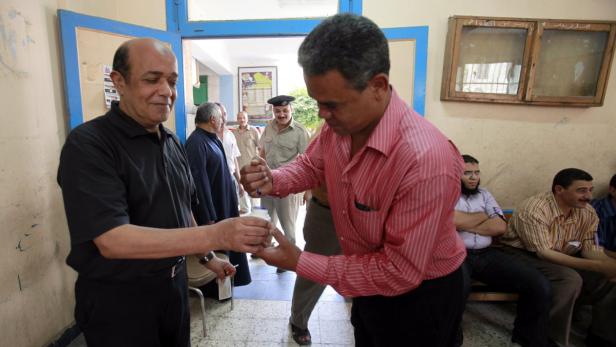 Zwei Männer tauschen etwas aus, möglicherweise bei einer Wahlveranstaltung.