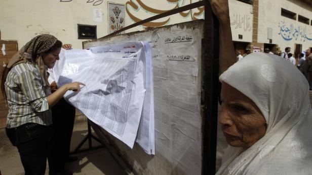 Frauen betrachten eine Liste mit Namen an einer Wand.