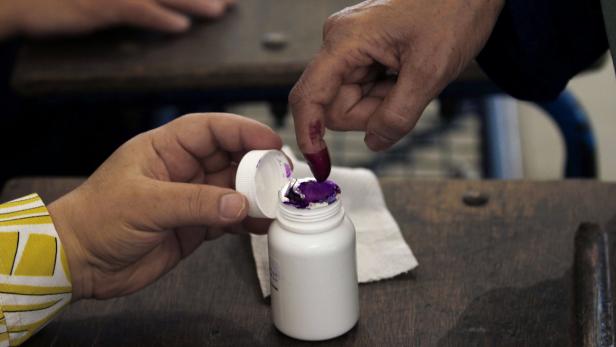 Eine Person taucht ihren Finger in ein Glas mit violetter Tinte.