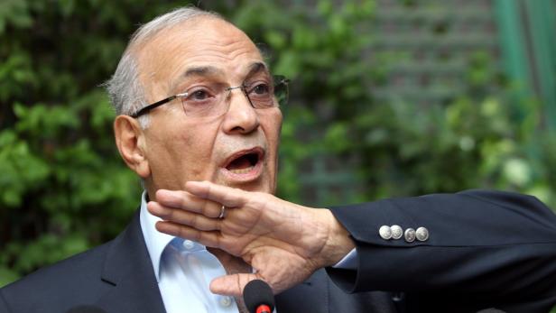 Ein älterer Mann mit Brille gestikuliert vor einem Mikrofon.