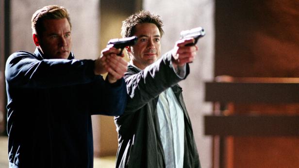 Val Kilmer und Robert Downey Jr. zielen mit Pistolen.