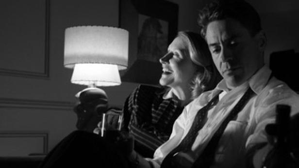 Ein Mann und eine Frau sitzen in einem Wohnzimmer, die Frau lacht.