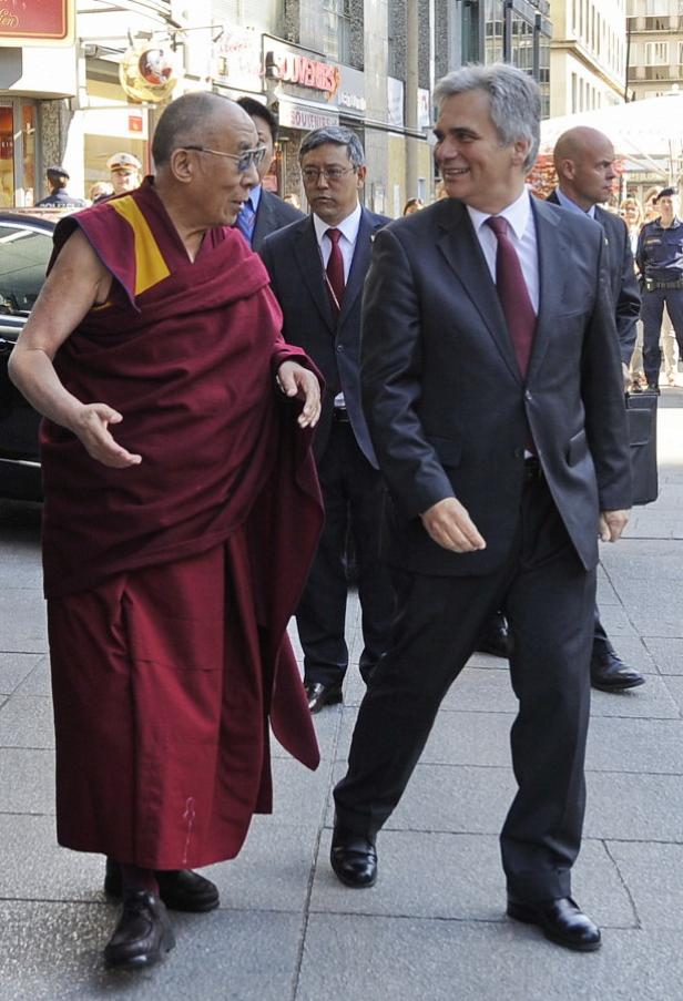 Der Dalai Lama geht mit einem Mann im Anzug auf der Straße entlang.