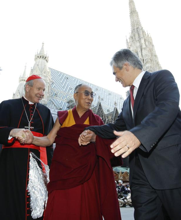 Der Dalai Lama wird von einem Kardinal und einem Mann im Anzug vor dem Stephansdom in Wien begrüßt.