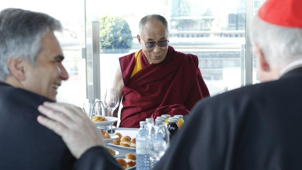 Der Dalai Lama sitzt mit anderen Personen an einem Tisch mit Speisen und Getränken.