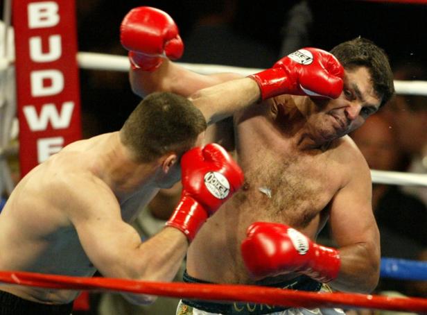 Ein Boxer schlägt seinen Gegner mit einem roten Boxhandschuh ins Gesicht.