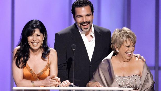 Drei Personen, darunter Edward James Olmos, lachen bei einer Preisverleihung.