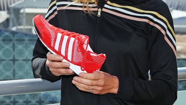 Eine Person hält einen roten Adidas-Schuh mit weißen Streifen in den Händen.