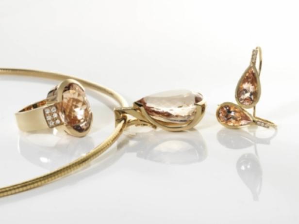 Ein goldenes Schmuckset mit Ring, Halskette und Ohrringen mit hellrosa Steinen.