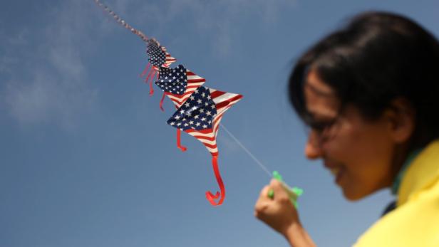 Eine Frau lässt eine lange Kette von Drachen mit dem Muster der US-Flagge steigen.