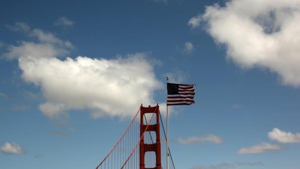 Die amerikanische Flagge weht vor einem blauen Himmel und einem Teil der Golden Gate Bridge.