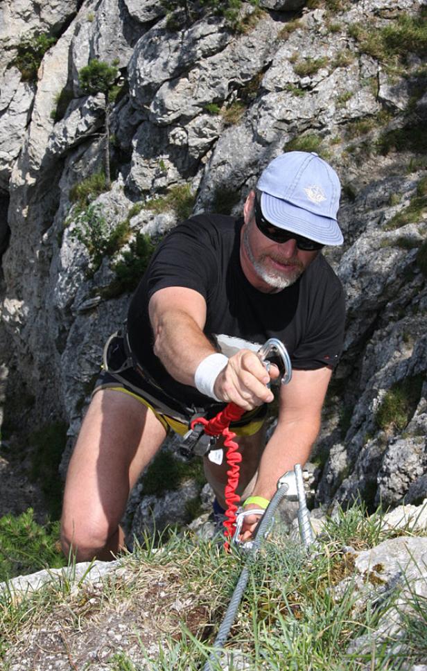 Ein Mann klettert einen Klettersteig in den Bergen hinauf.