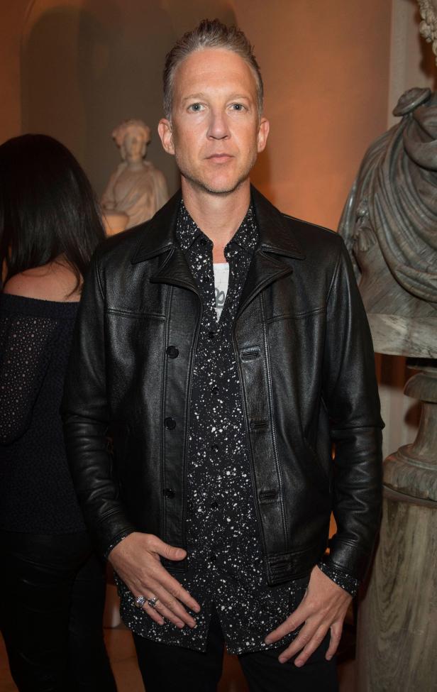 Ein Mann mit Lederjacke posiert vor einer Marmorbüste.