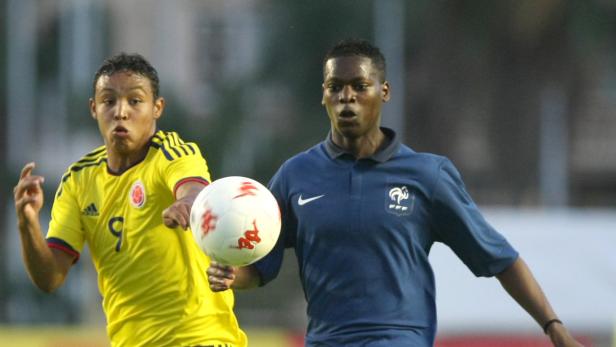 Zwei Fußballspieler, einer im gelben Trikot Kolumbiens und einer im blauen Trikot Frankreichs, kämpfen um den Ball.